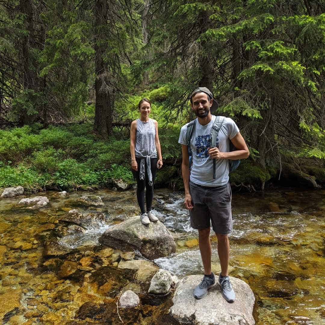 Hiking outdoors in a green forest with two smiling people standing on rocks.